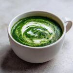 Close-up of a bowl of vibrant green spinach soup topped with a white cream swirl.