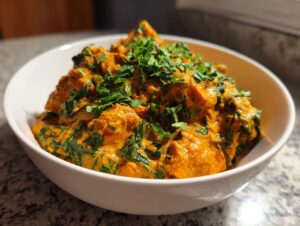 A close-up of a hearty serving of rich, orange pumpkin curry mixed with spinach, topped with fresh cilantro in a white bowl.
