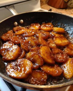 Close-up of thick, caramelized apple pie filling simmering in a dark skillet on a stovetop.