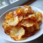A close-up of a white bowl filled with golden brown, seasoned air fryer potato chips.