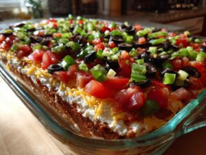 Close-up of a rectangular glass dish filled with a vibrant 7 layer dip, topped with tomatoes, olives, and green onions.