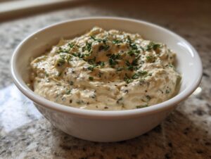 A creamy, textured olive dip topped with fresh chopped chives served in a white bowl.