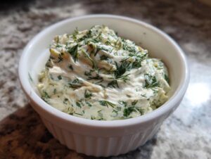 Close-up of creamy, herbed pickle dip swirled in a small white ramekin.