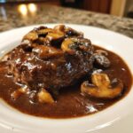 A close-up of a perfectly cooked salisbury steak smothered in rich brown mushroom gravy.