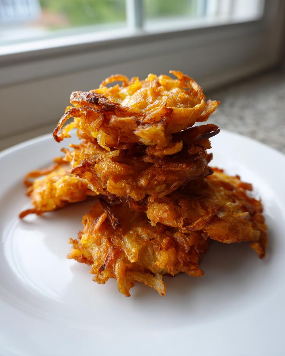 A stack of crispy, golden brown Amish Onion Fritters piled high on a white plate.