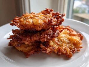 A stack of three perfectly golden brown, crispy Amish Onion Fritters resting on a white plate.
