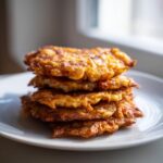 A stack of four golden-brown, crispy Amish Onion Fritters piled on a white plate.