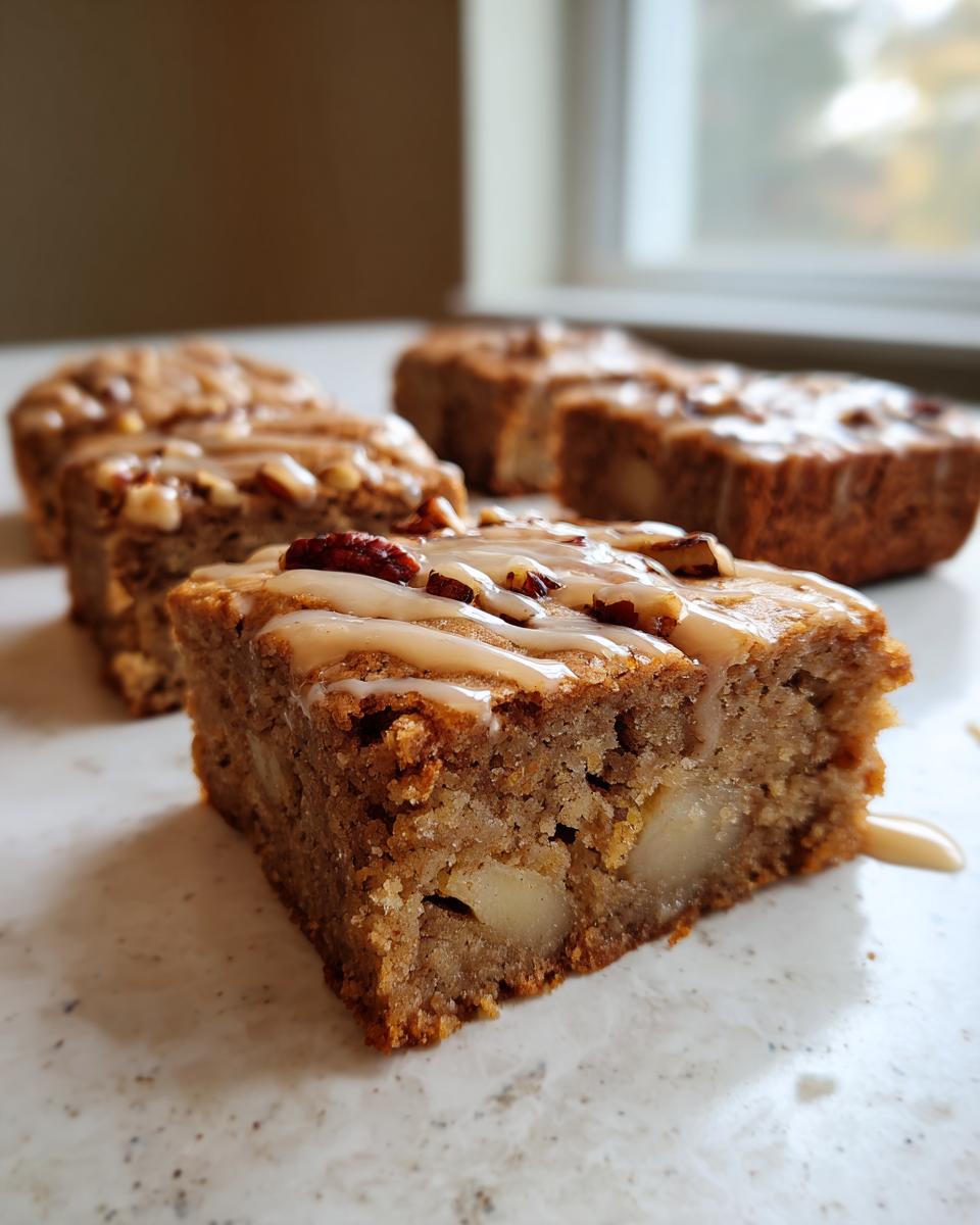 A close-up of a square apple brownies slice, showing chunks of apple inside and topped with a caramel glaze and pecans.