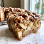 Close-up of a moist slice of apple brownies loaded with chunks of apple, topped with pecans and caramel drizzle.