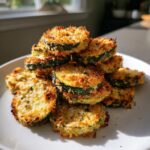 A stack of crispy, golden brown baked parmesan zucchini slices piled high on a white plate.