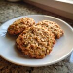 Close-up of three golden brown banana oatmeal cookies resting on a white plate.
