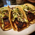 Three delicious salmon tacos filled with blackened salmon pieces and topped with fresh cabbage slaw.