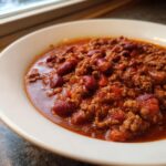 Close-up of a white bowl filled with rich, thick high protein chili featuring ground meat and dark red kidney beans.