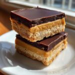 Two stacked bars of buckeye graham crackers dessert featuring a crust, peanut butter layer, and chocolate topping.