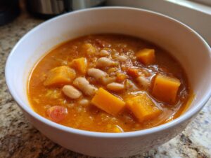 Close-up of a white bowl filled with thick, orange butternut squash chili featuring large chunks of squash and white beans.