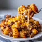 A fork lifts a bite of Cheesy Taco Potatoes covered in melted, stretching cheese and seasoned ground beef.