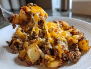 A fork lifts a bite of Cheesy Taco Potatoes, showing browned potatoes, seasoned ground meat, and gooey, melted cheddar cheese.