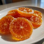 Close-up of glistening, bright orange candied orange slices heavily coated in sparkling white sugar crystals.