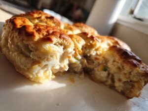 Close-up of a serving of chicken pot pie casserole showing the creamy filling and golden, flaky biscuit crust.