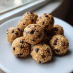 A close-up of several homemade chocolate chip protein balls stacked on a white plate.