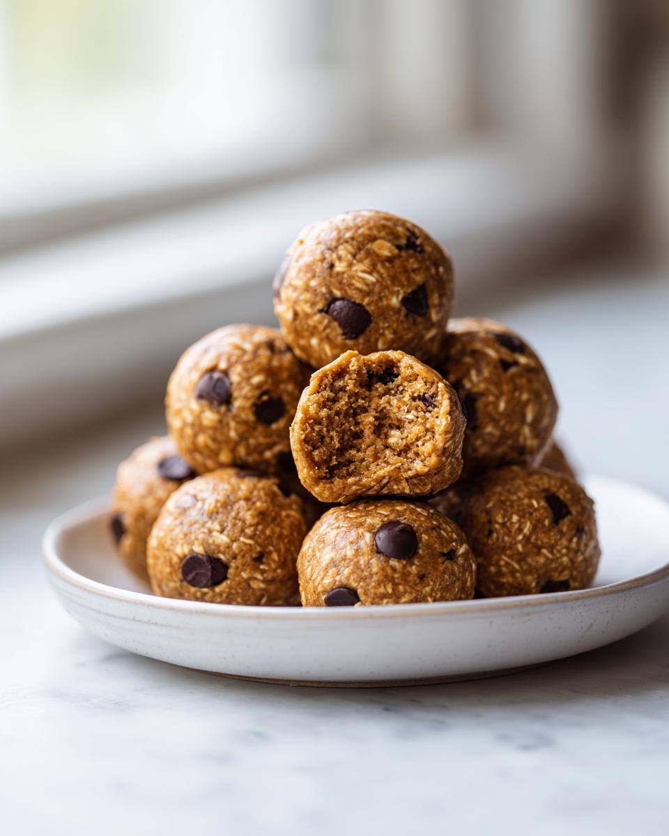 A stack of homemade chocolate chip protein balls on a small white plate, with one ball bitten in half showing the texture.