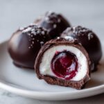 A close-up of a chocolate covered cherries treat cut in half, revealing the white filling and dark cherry center.