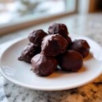 A stack of rich, chocolate-covered Oreo balls on a white plate, with one center ball broken open to show the dark filling.