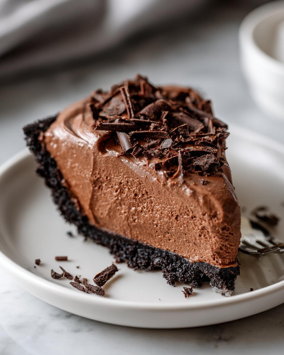 A decadent slice of chocolate mousse pie with a dark crust, topped with chocolate shavings.