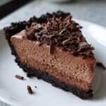 A decadent slice of chocolate mousse pie featuring a dark crust and topped with generous chocolate shavings.