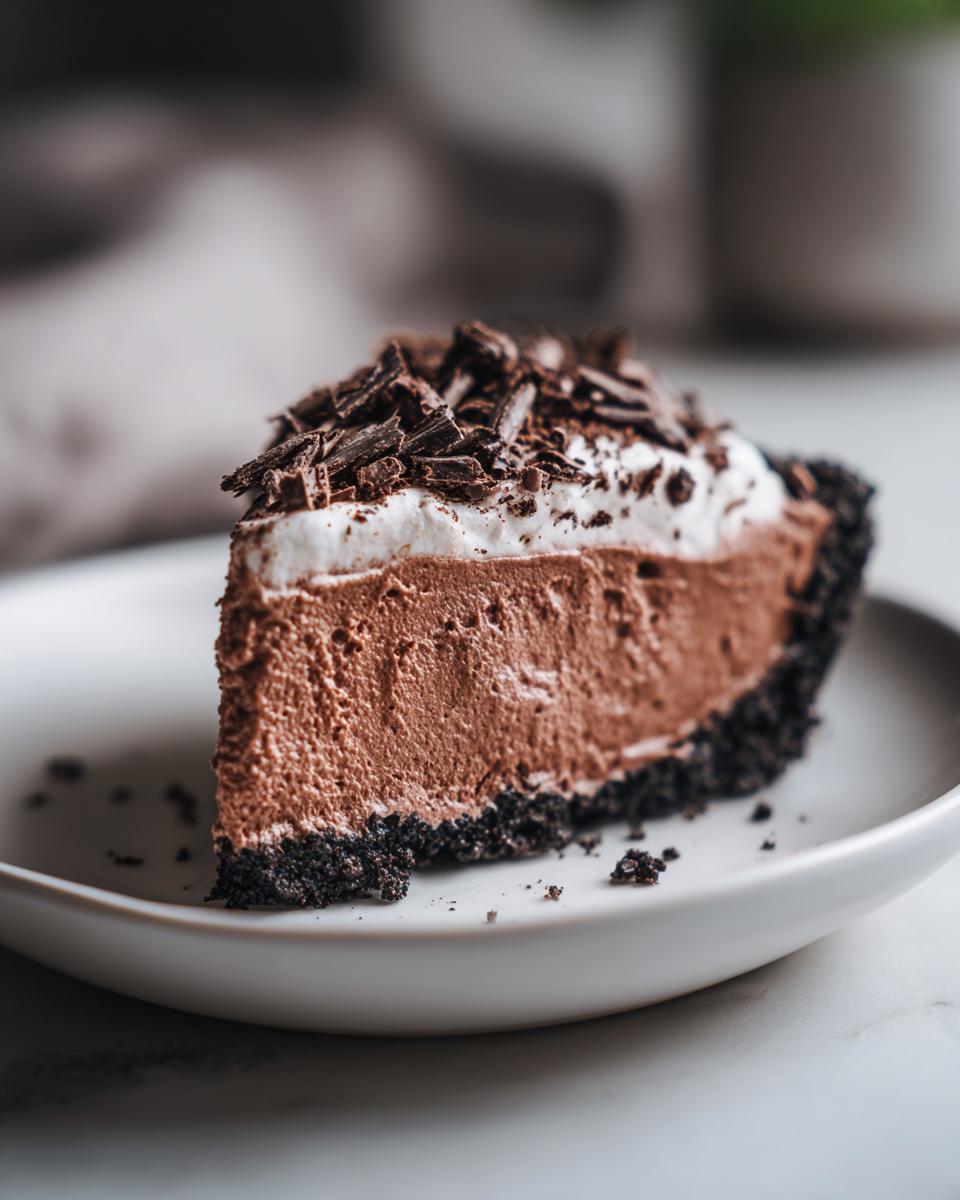 A perfect slice of rich chocolate mousse pie with a dark crust, whipped topping, and chocolate shavings.
