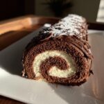 A cross-section view of a chocolate yule log cake showing the dark chocolate sponge rolled with white cream filling.