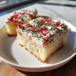 Two squares of soft christmas sugar cookie bars topped with white frosting and red and green holiday sprinkles.
