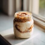 A jar of creamy overnight oats swirled with cinnamon filling, ready for breakfast.