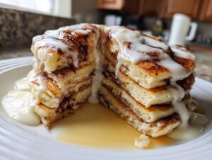 A tall stack of cinnamon roll pancakes, cut in half, generously topped with white icing and syrup.
