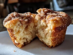 A close-up view of a cinnamon sugar french toast muffin broken in half, showing the soft interior and sugary topping.