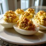 Close-up of several perfectly piped deviled eggs sprinkled with paprika on a white plate.