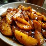 Close-up of thick, glossy slices of apple pie filling coated in a rich, spiced brown sauce.