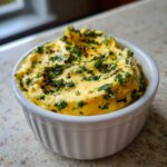 Close-up of rich, yellow cowboy butter dipping sauce topped with fresh green herbs and red pepper flakes in a white bowl.