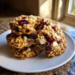 A stack of four delicious cranberry oatmeal cookies featuring visible dried cranberries and white chocolate chips.