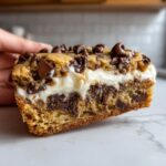 A thick, decadent slice of cookie cake recipe filled with creamy white frosting and loaded with chocolate chips.