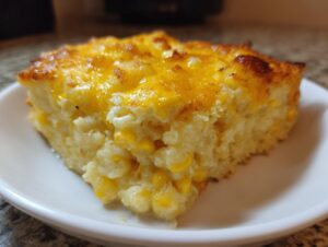 A close-up of a moist slice of cream cheese corn casserole topped with golden melted cheddar cheese.