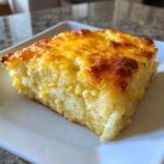 A square slice of creamy cream cheese corn casserole with a golden, baked cheese topping.