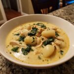 A close-up of a bowl of creamy chicken gnocchi soup featuring tender chicken, spinach, and potato dumplings.