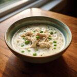 A close-up of a hearty bowl of homemade cream of chicken soup topped with shredded chicken and bright green peas.