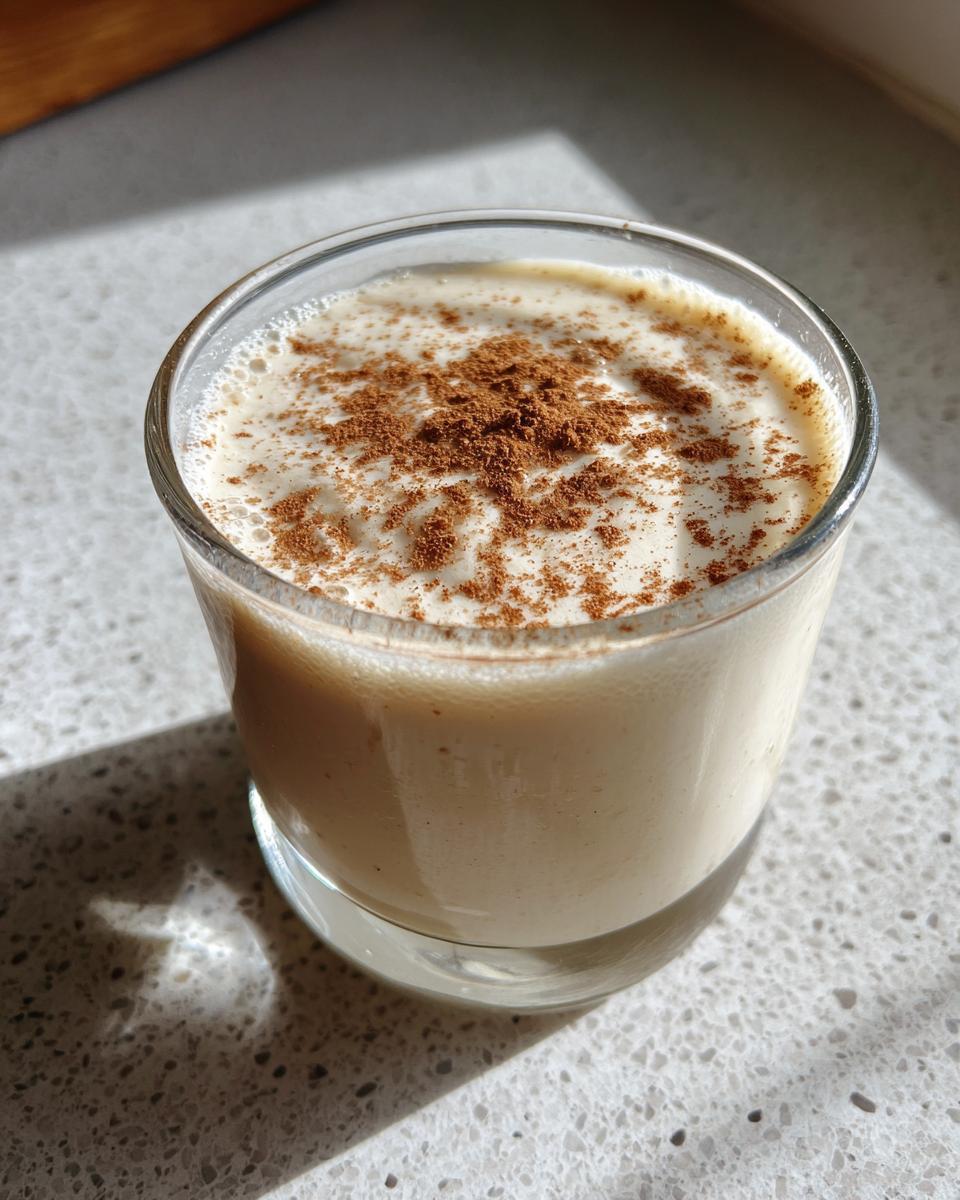 Close-up of a creamy glass of coquito topped generously with ground cinnamon.