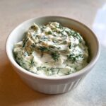 Close-up of creamy dill dip mixed with fresh green dill, served in a small white ramekin.