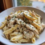 Close-up of creamy garlic parmesan chicken pasta with penne, topped with black pepper and parsley.