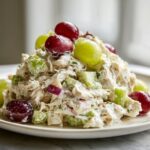 A close-up of creamy greek yogurt chicken salad mixed with celery, red onion, and topped with red and green grapes.