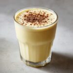A tall glass filled with creamy homemade eggnog, topped with a dusting of cinnamon or nutmeg.