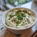 A close-up of a creamy, light-colored olive dip garnished generously with chopped fresh chives.
